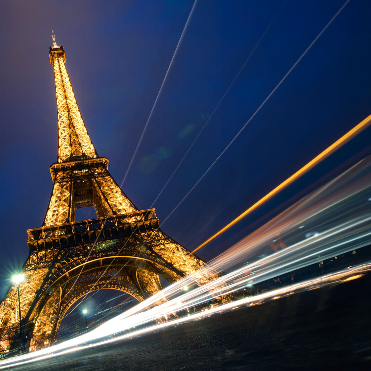 Night time view of the eiffel tower with light trails from passing vehicles.