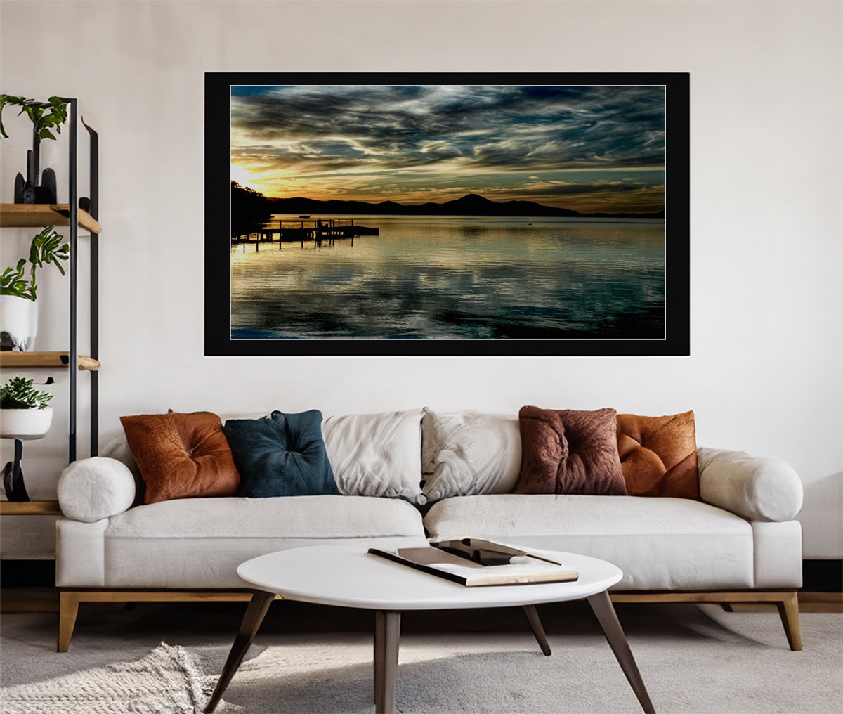 Golden sunset over a serene lake with silhouettes of a pier and distant mountains under a dramatic sky.